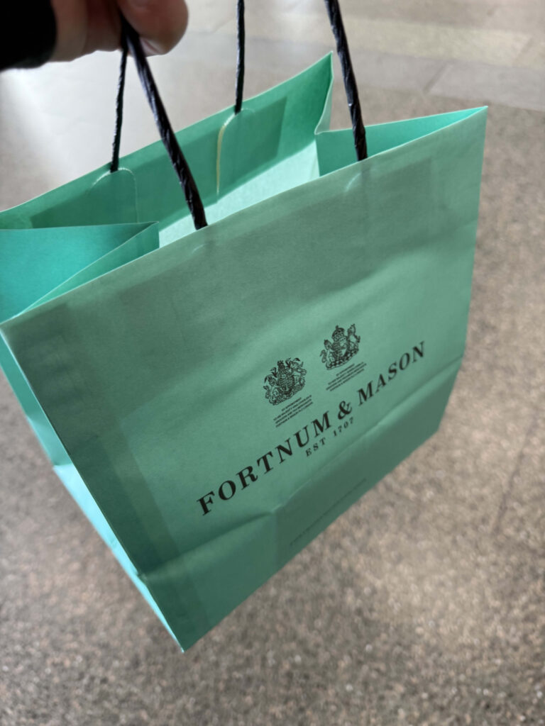 A hand holding a Fortnum & Mason shopping bag in the signature Eau de Nil color