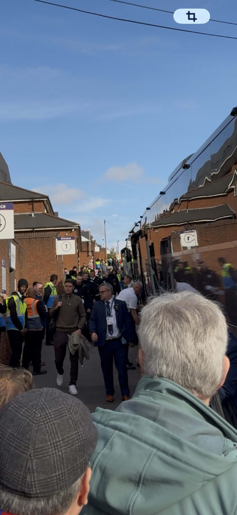 Brighton & Hove Albion manager Fabian Hürzeler walking past the team bus and security guards outside a stadium entrance.