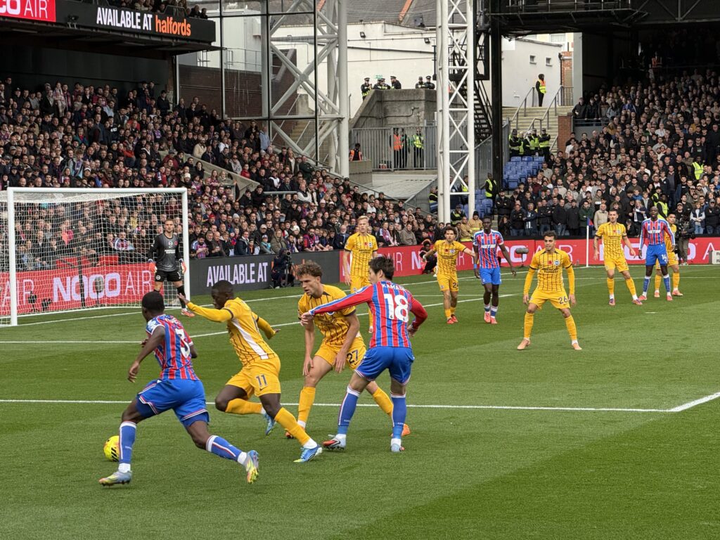 Crystal Palace's Daichi Kamada, wearing the number 18 jersey, playing on the field surrounded by opposing players in yellow kits during a soccer match.