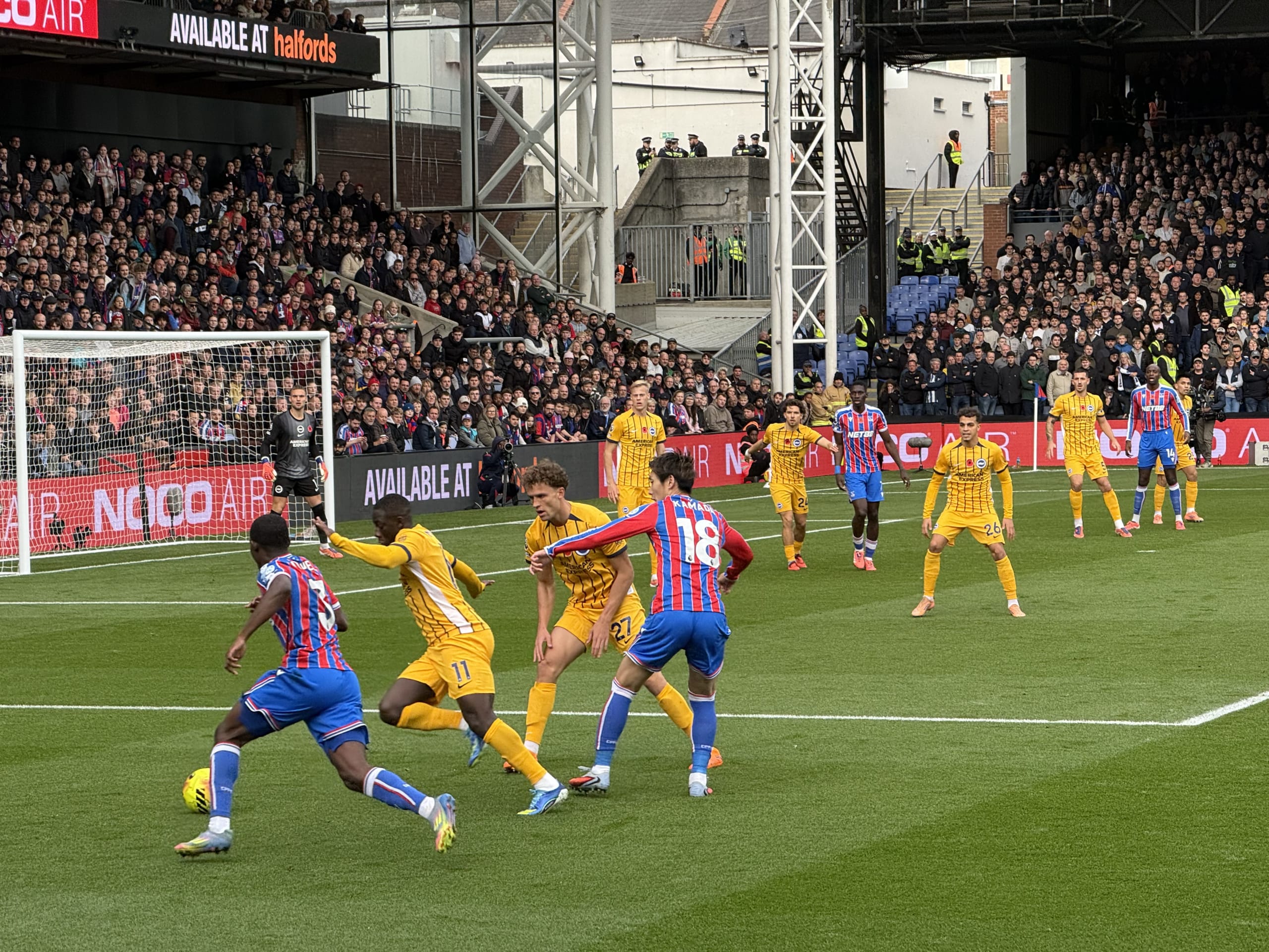 Crystal Palace's Daichi Kamada, wearing the number 18 jersey, playing on the field surrounded by opposing players in yellow kits during a soccer match.