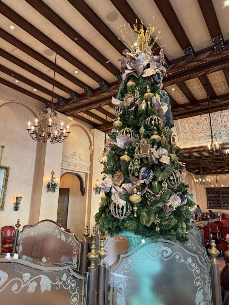 A lavish Christmas tree decorated with gold and bronze ornaments standing inside a spacious restaurant with high ceilings