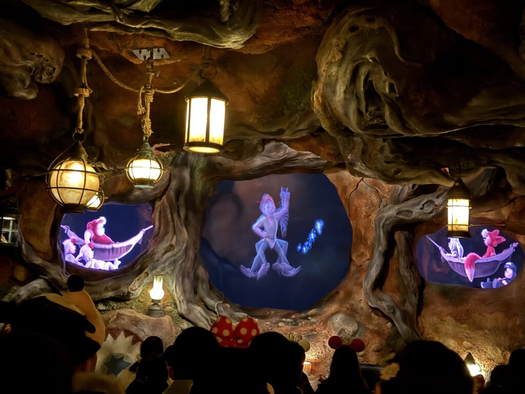 ディズニーのアトラクション「ピーターパン空の旅」の内部。洞窟のような隠れ家でランタンが灯り、奥にピーターパンの光る影とロストボーイズが見える