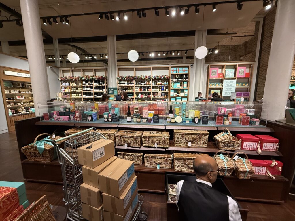 フォートナム・アンド・メイソンの店内で、ハンパーや紅茶が並ぶ棚の前で品出し作業をする店員と段ボール箱