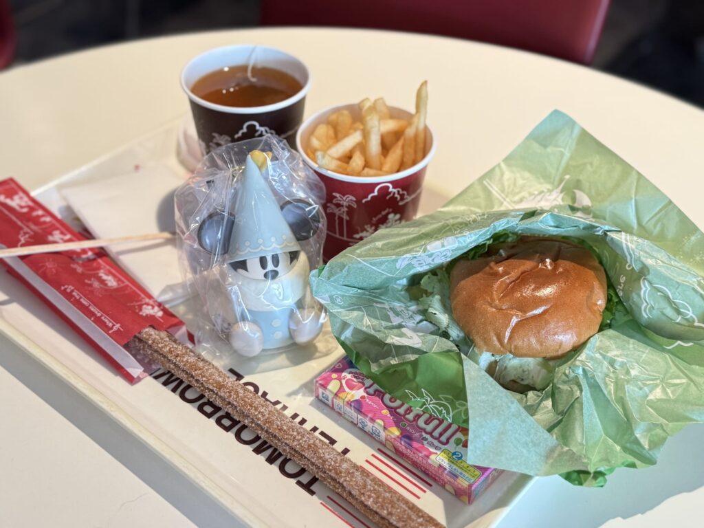 A food tray at Tomorrowland Terrace featuring a burger, churro, fries, and the mobile-order exclusive blue Li'l RingRing mini snack case