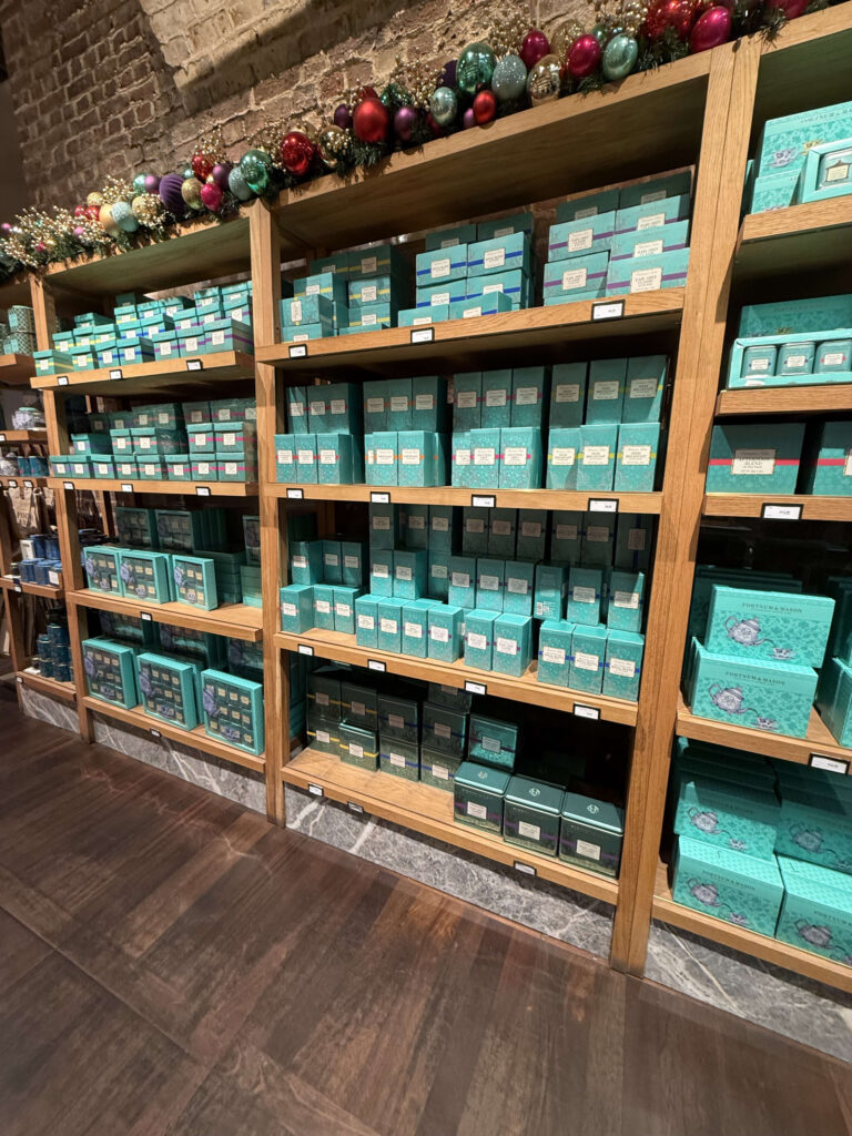 Wooden shelves neatly stacked with emerald green Fortnum & Mason tea boxes topped with Christmas garland decorations