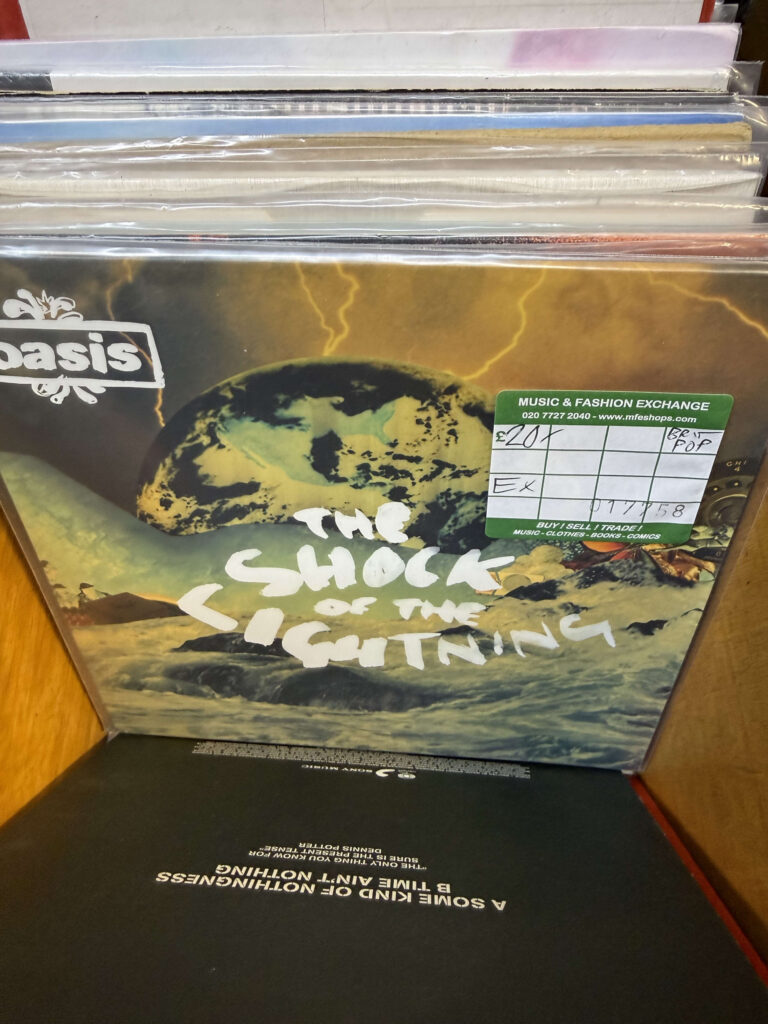 Oasis 'The Shock of the Lightning' 7-inch vinyl record in a store bin with a price tag
