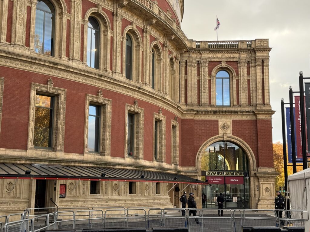 ロンドンのロイヤル・アルバート・ホールの外観。赤レンガと装飾的な石造りの壮麗な建物の入り口付近に、複数の警察官が立っている。