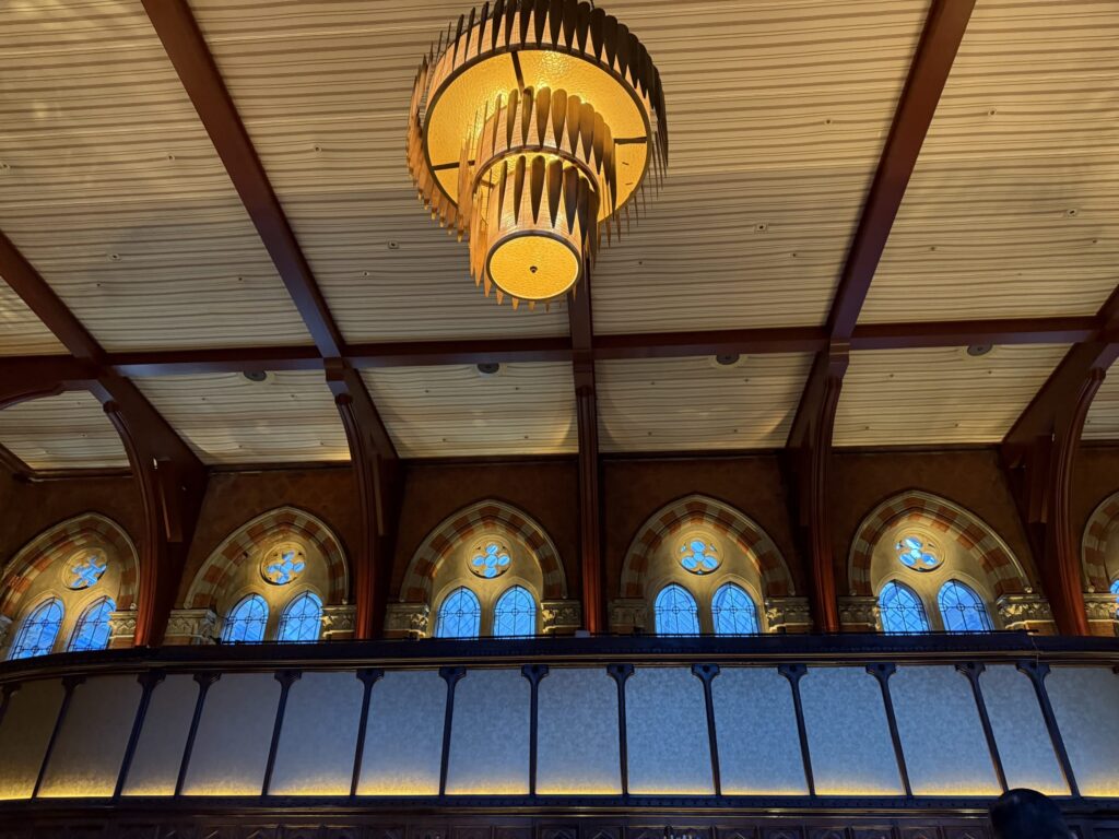 Large golden tiered chandelier hanging from a beamed ceiling at Booking Office 1869 with arched windows in the background