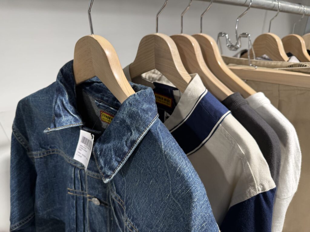 Human Made denim jacket hanging on a wooden hanger along with other clothes on a rack