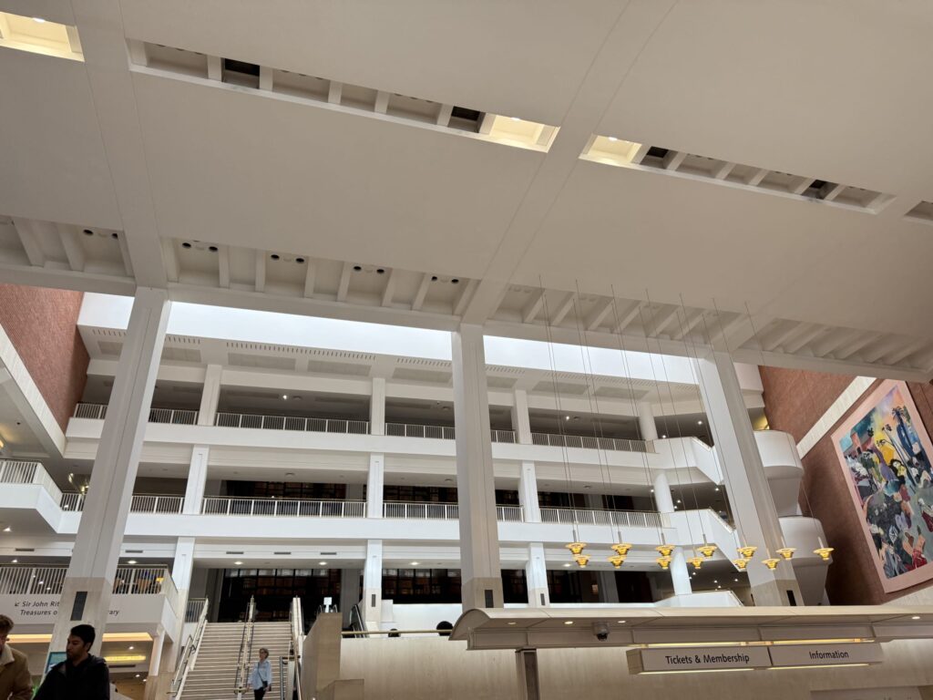 高い天井と白い柱が特徴的な広々とした吹き抜け、吊り下げられた照明、赤レンガの壁、正面のインフォメーションカウンター