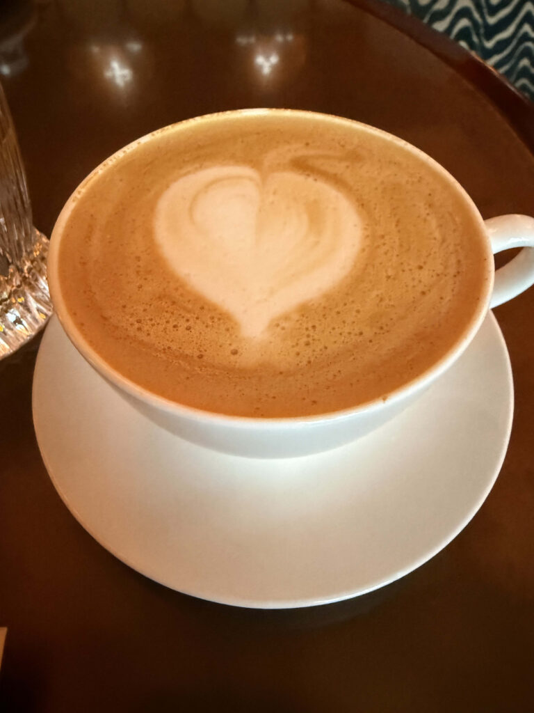 Almond milk latte with heart-shaped latte art in a white cup on a dark wooden table