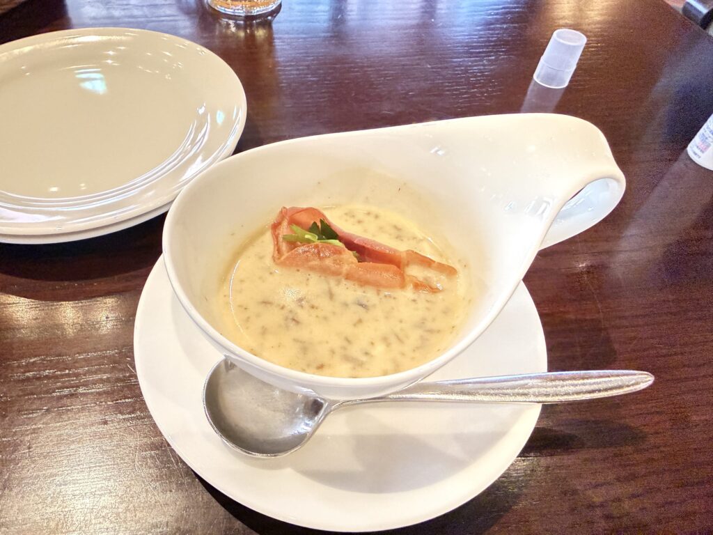 Creamy mushroom soup with truffle aroma garnished with prosciutto served in a unique curved white bowl