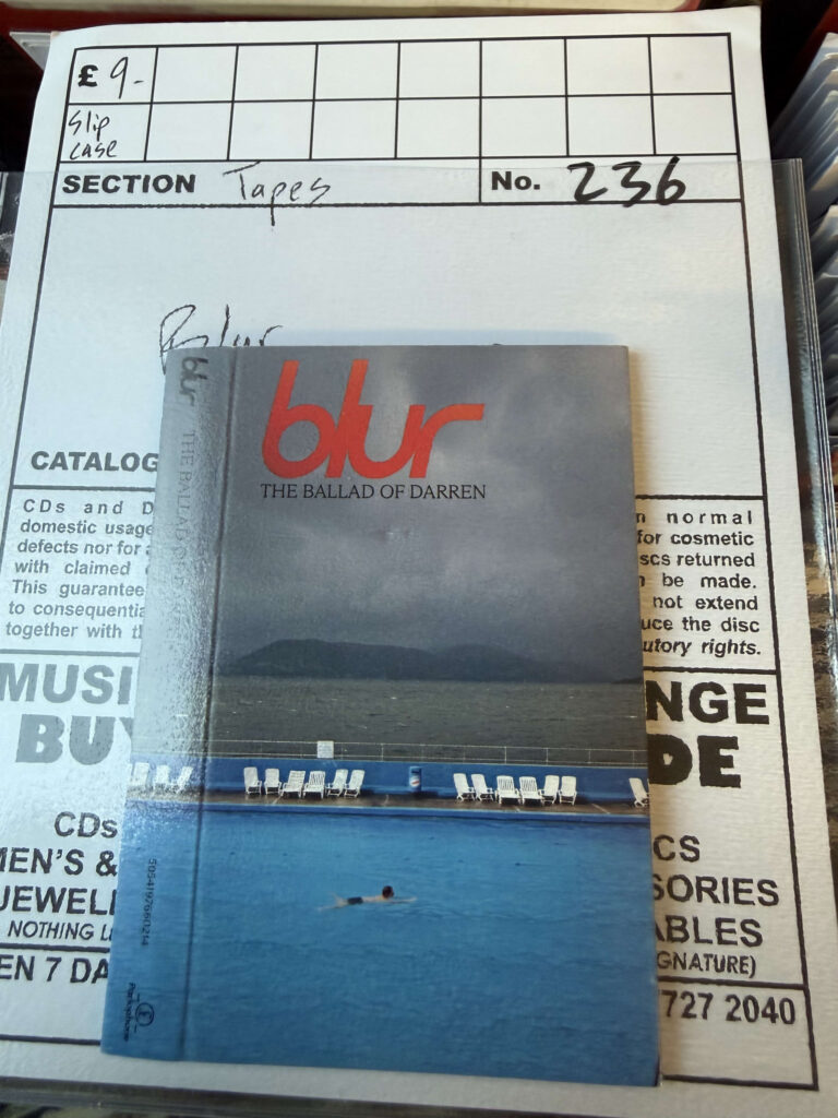 Cassette tape of Blur's album 'The Ballad of Darren' sitting on a handwritten shop inventory card