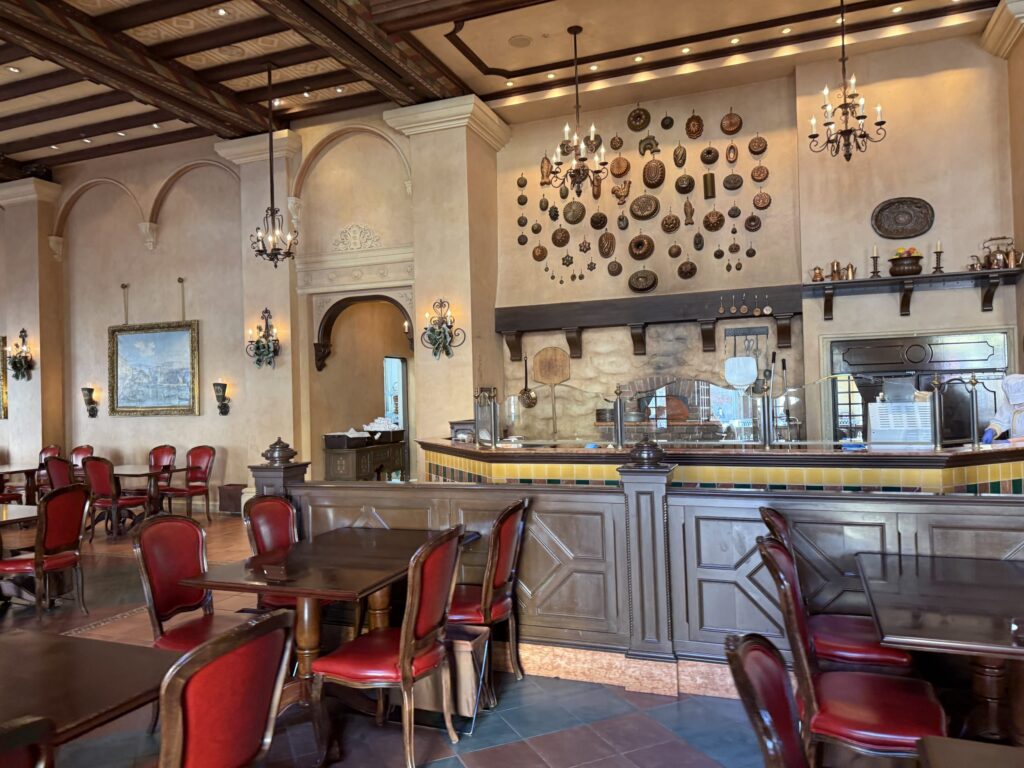 Interior of a rustic Italian-style restaurant with red chairs, wooden tables, and a wall covered in antique baking molds