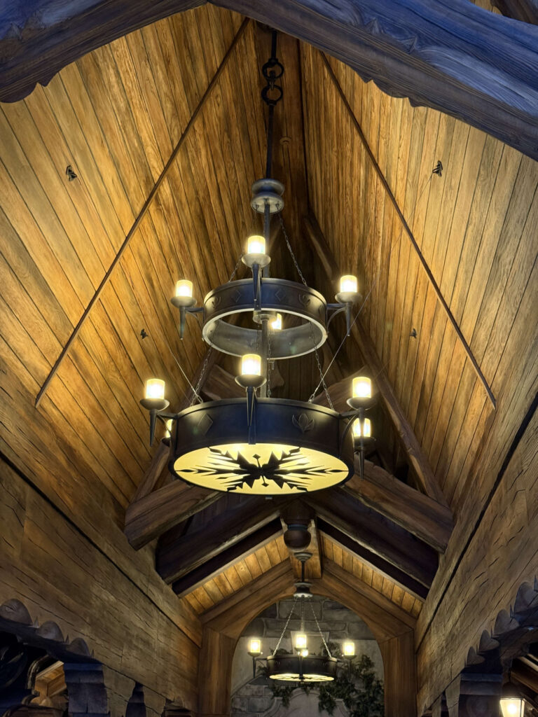 A two-tiered black iron chandelier with a snowflake-like pattern on the bottom hanging from a high wooden vaulted ceiling.