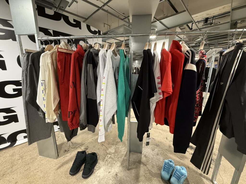 Clothing rack displaying C.E (Cavempt) streetwear collection including hoodies, jackets, and sneakers