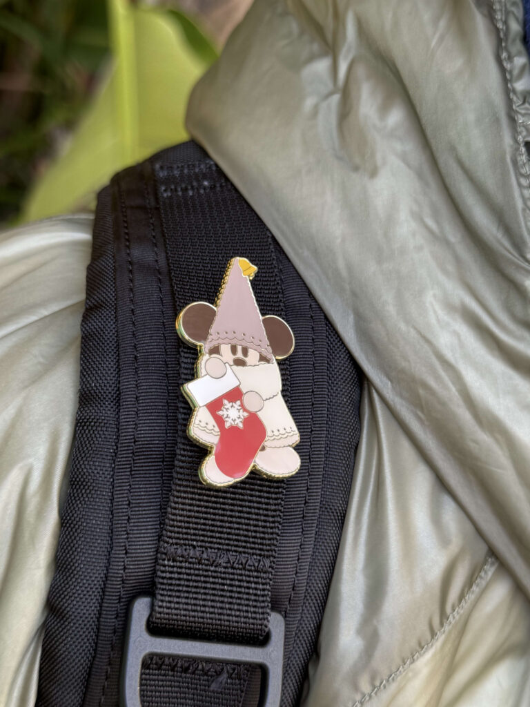 Close-up of a Li'l RingRing enamel pin attached to a black backpack strap, featuring the character holding a red Christmas stocking