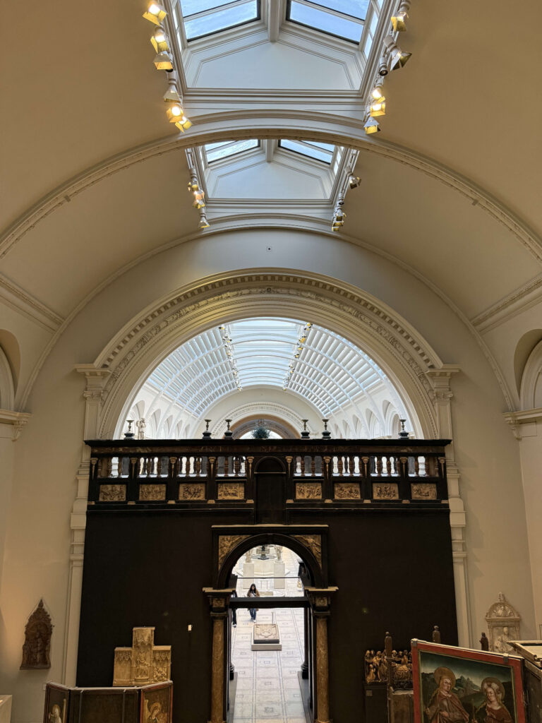 The interior of a museum with a high, arched ceiling. In the center is a large, carved wooden structure, with another gallery visible through its archway.