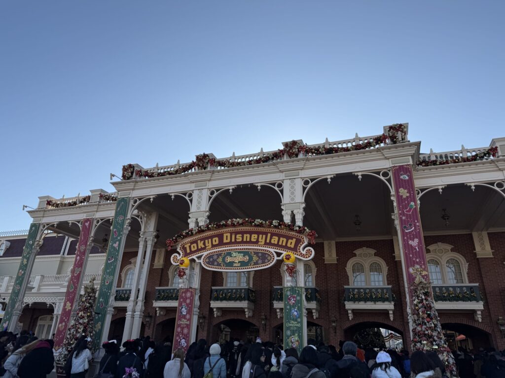 快晴の青空の下、クリスマスの装飾が施された東京ディズニーランドのワールドバザール入り口と、入場する多くの人々