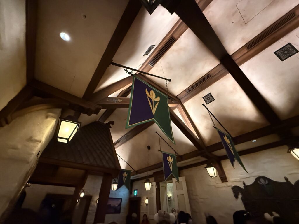 Arendelle flags with the gold crocus crest on purple and green backgrounds hanging from a high wooden ceiling with beams and lanterns