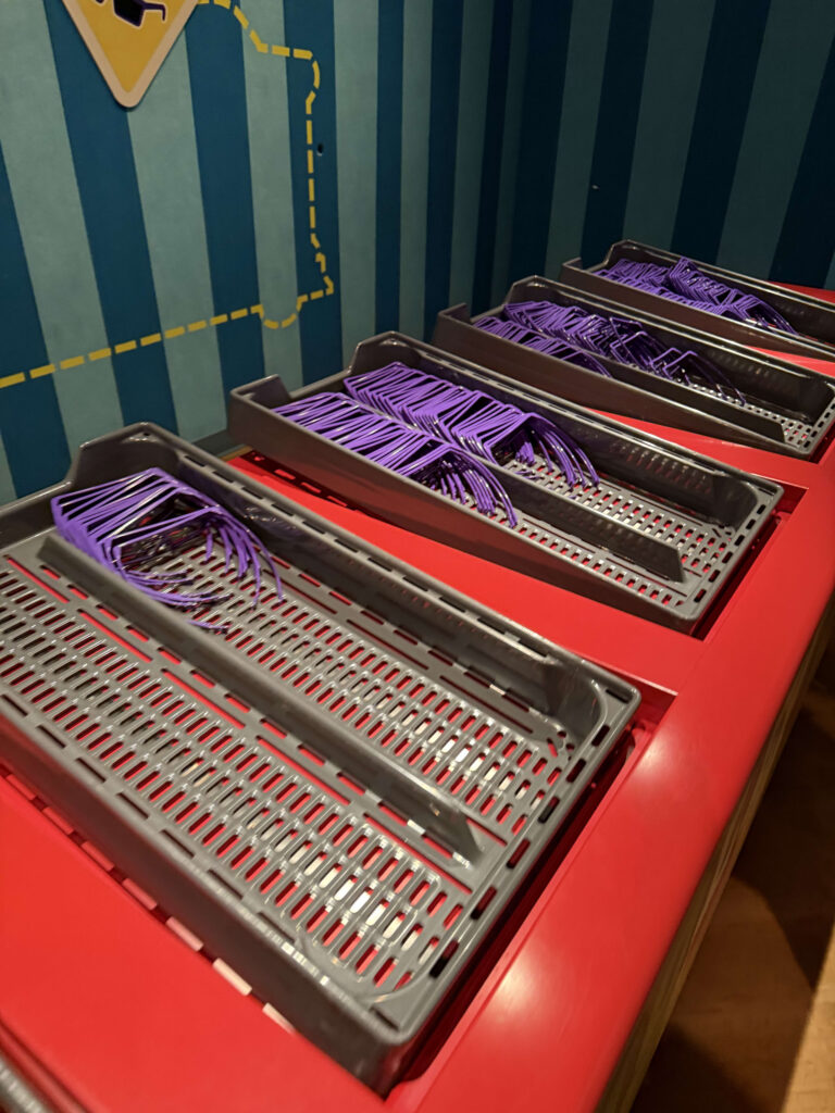 赤い台の上に並べられた、紫色の3Dメガネが入ったグレーのトレイ