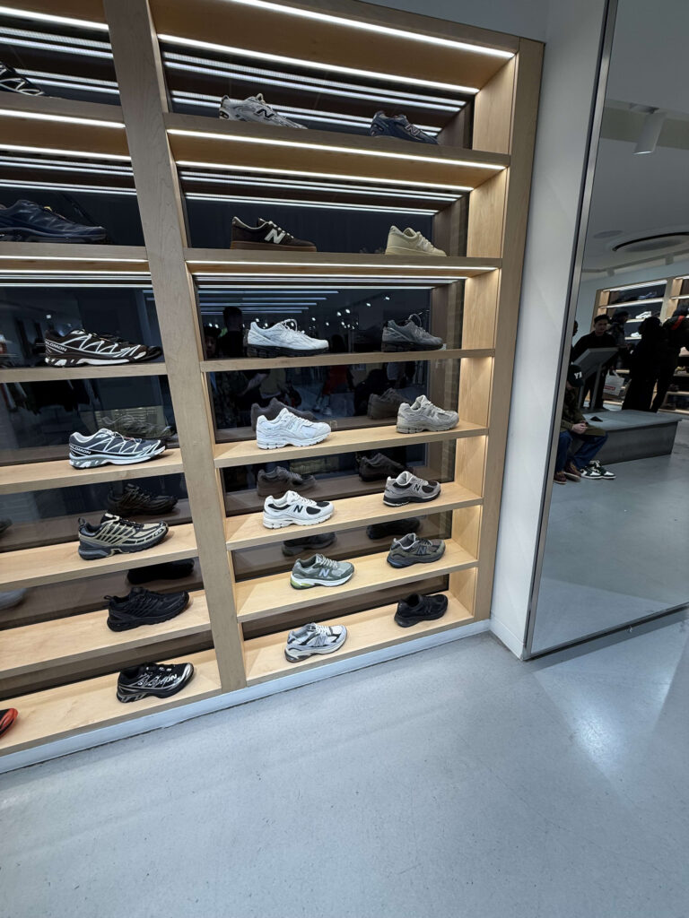 Wooden display shelves in a store neatly arranged with sneakers from brands like New Balance and Salomon