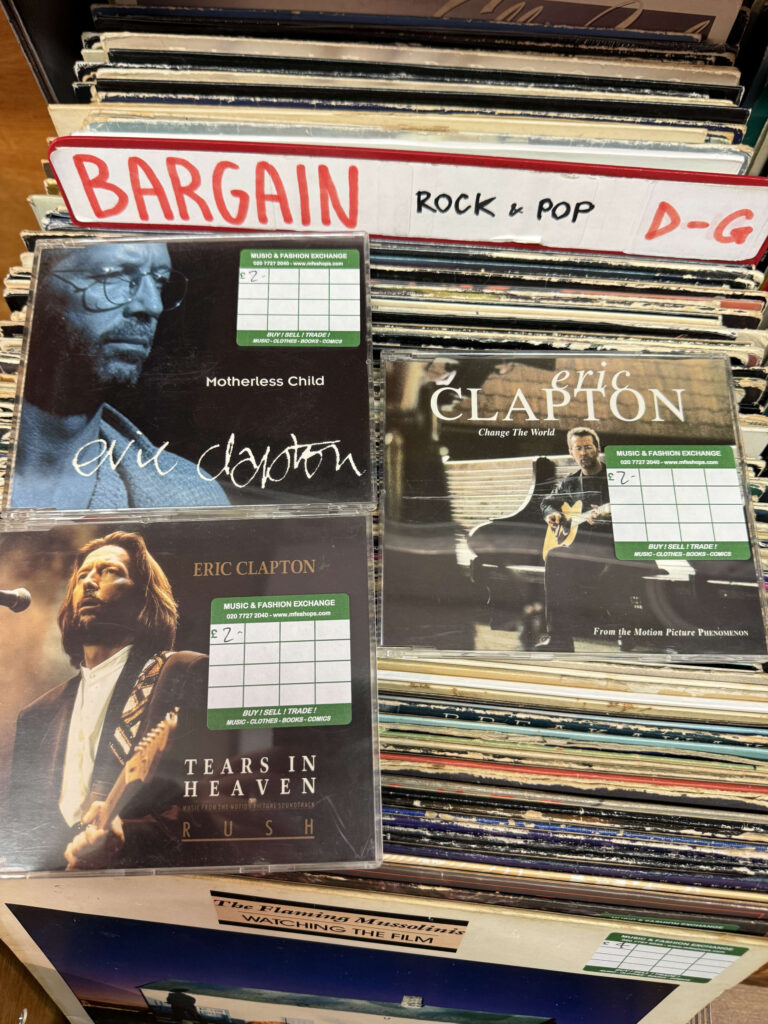 中古レコード店のバーゲンコーナーでレコードの山の上に置かれた、エリック・クラプトンのシングルCD3枚（Motherless Child、Change The World、Tears in Heaven）