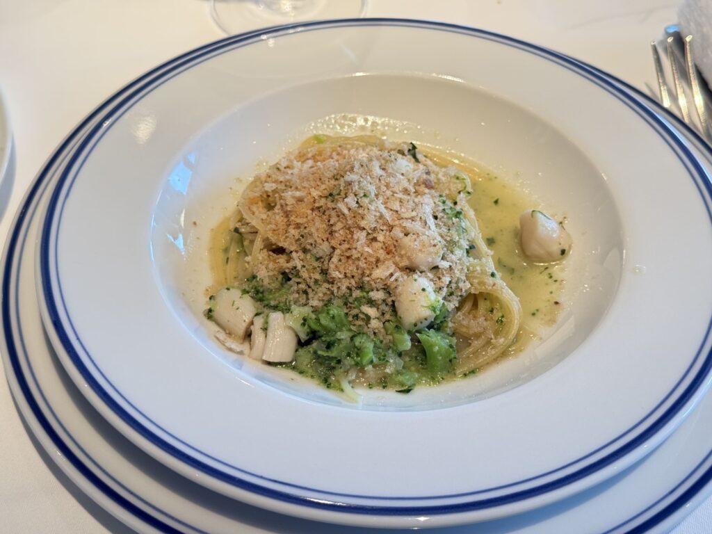 Spaghettini with broccoli and baby scallops served on a blue-rimmed plate, topped with golden anchovy-flavored breadcrumbs.