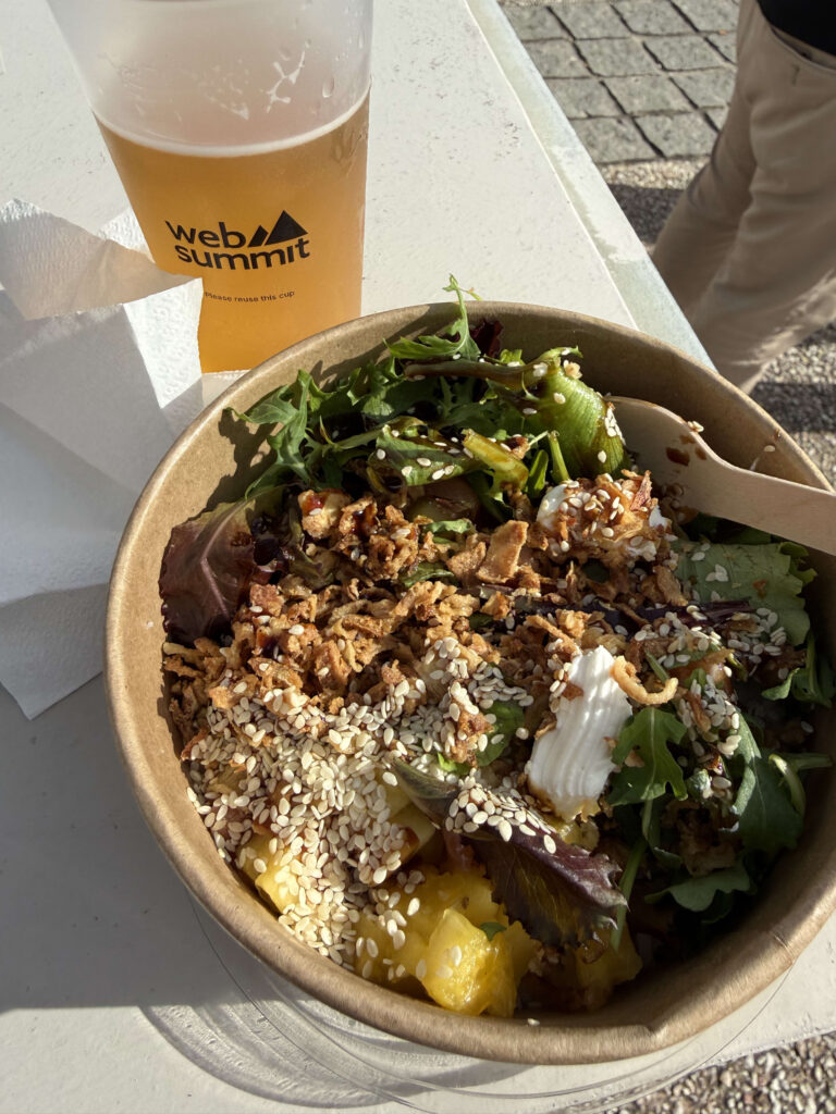 A vegetarian poke bowl topped with sesame seeds and crispy onions next to a plastic cup of beer with the Web Summit logo