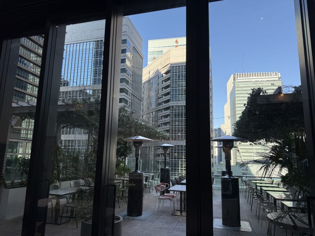 Urban terrace with patio heaters and dining tables surrounded by skyscrapers viewed through a large window.