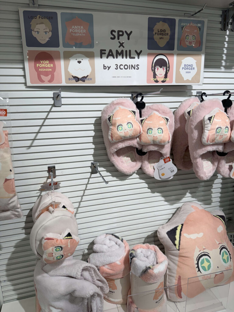 SPY x FAMILY collaboration merchandise display at 3COINS featuring Anya slippers, cushions, and blankets.