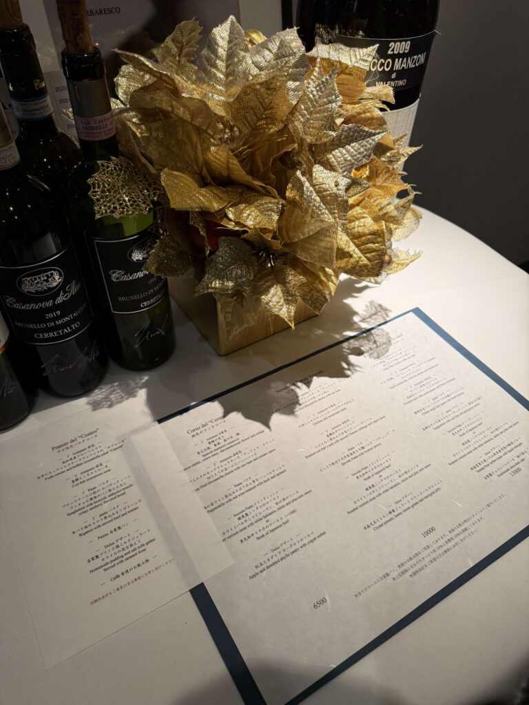 Restaurant table setting featuring wine bottles, a golden poinsettia decoration, and the printed menu for the weekday limited pasta course.