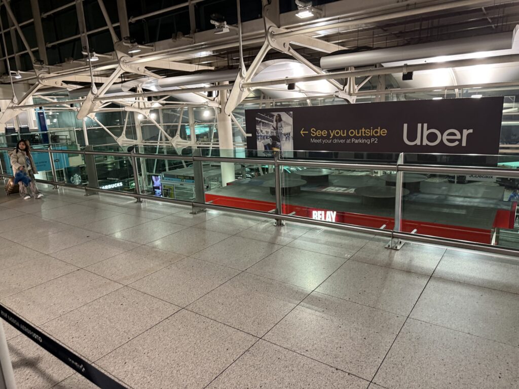 リスボン空港の吹き抜けにある大きなUberの案内看板と、ガラスの手すり越しに見える空港内部の様子