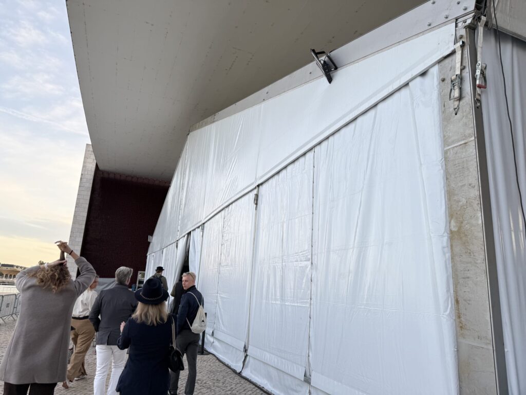 People walking alongside a massive white tent structure set up under a concrete overhang