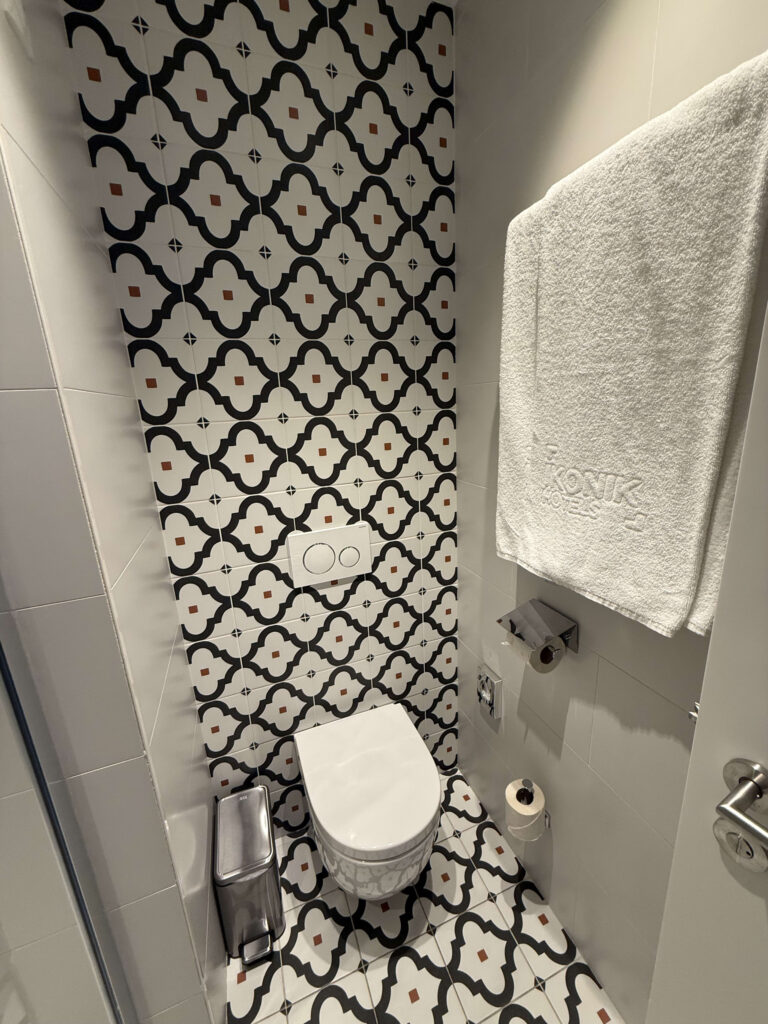 A modern, clean hotel toilet room featuring black and white geometric tiles and a branded white towel.