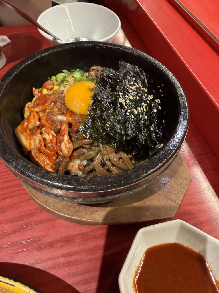 Hot stone bowl bibimbap topped with raw egg yolk, kimchi, seasoned seaweed, and vegetables on a red table