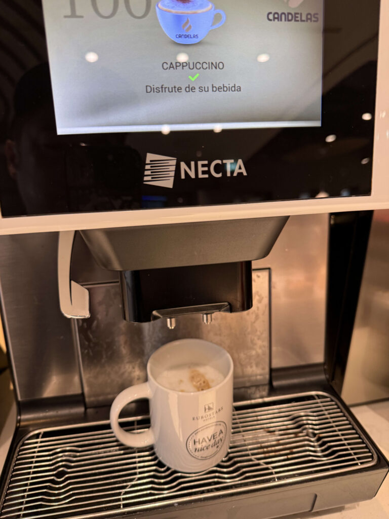 NECTA製コーヒーマシンの画面と、抽出されたカプチーノが入ったユーロスターズホテルのマグカップ