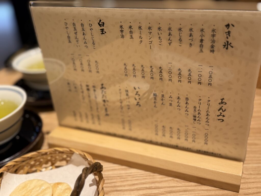 Close-up photo of a Japanese cafe menu listing Kakigori shaved ice, Anmitsu, and Shiratama dumplings