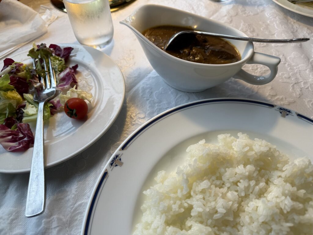 白いテーブルクロスの上に置かれたソースポット入りのカレー、ライス、食べかけのサラダ