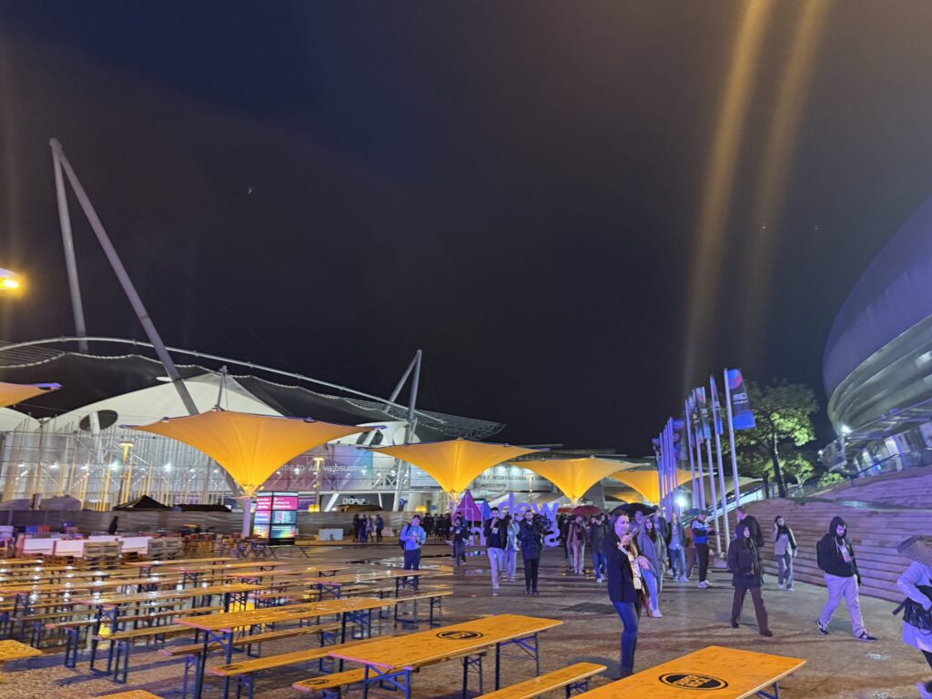 Web Summit会場の夜景。ライトアップされた黄色い傘型のキャノピーと雨に濡れた地面に反射する光