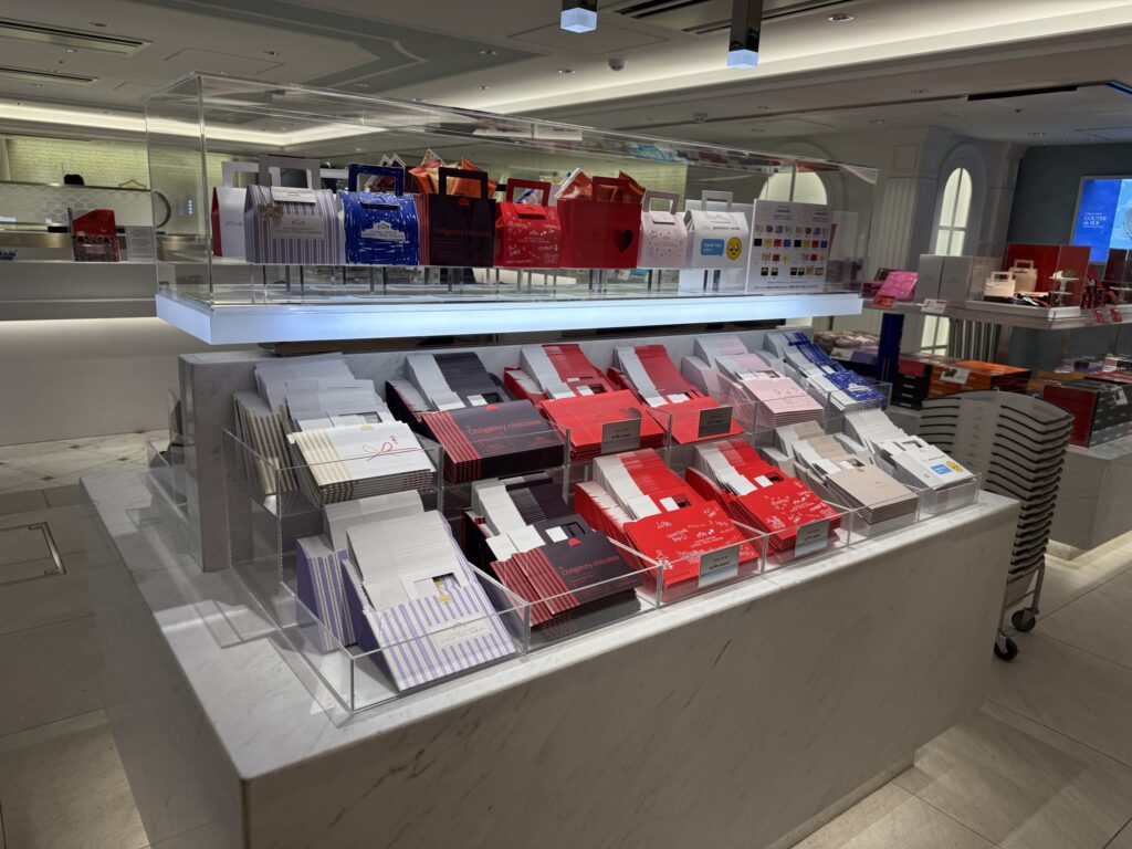 Display of customized gift packages at the Tokyo Station store, featuring envelopes with messages like 'Obligatory chocolate' and various colorful designs arranged on shelves.