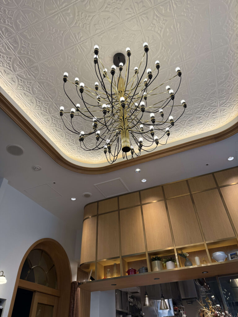 Parisian bistro-style interior with white geometric ceiling tiles and a modern brass chandelier