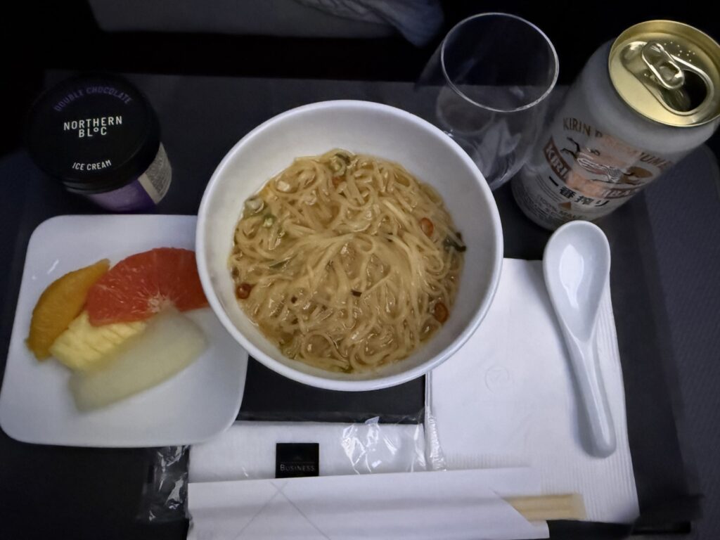機内のテーブルに置かれた九州じゃんがらラーメン、カットフルーツ、アイスクリーム、キリン一番搾りの缶ビール
