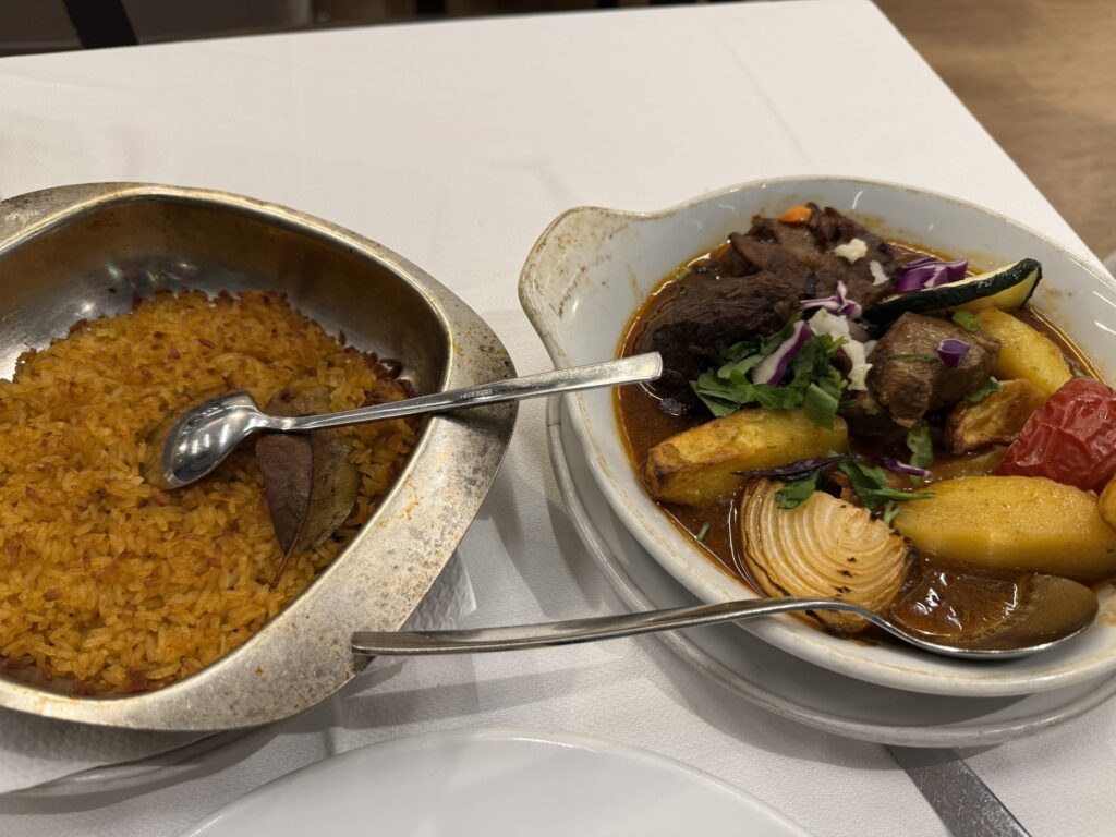 Oven-baked veal with vegetables in a traditional sauce and a side of yellow rice served on a white tablecloth