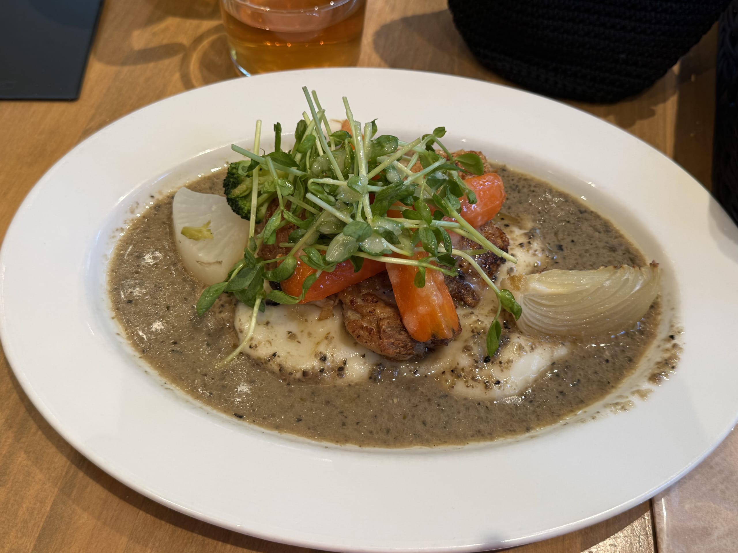 Poêlé of chicken thigh served in a creamy grainy mustard sauce with roasted carrots, onions, and fresh greens on a white plate