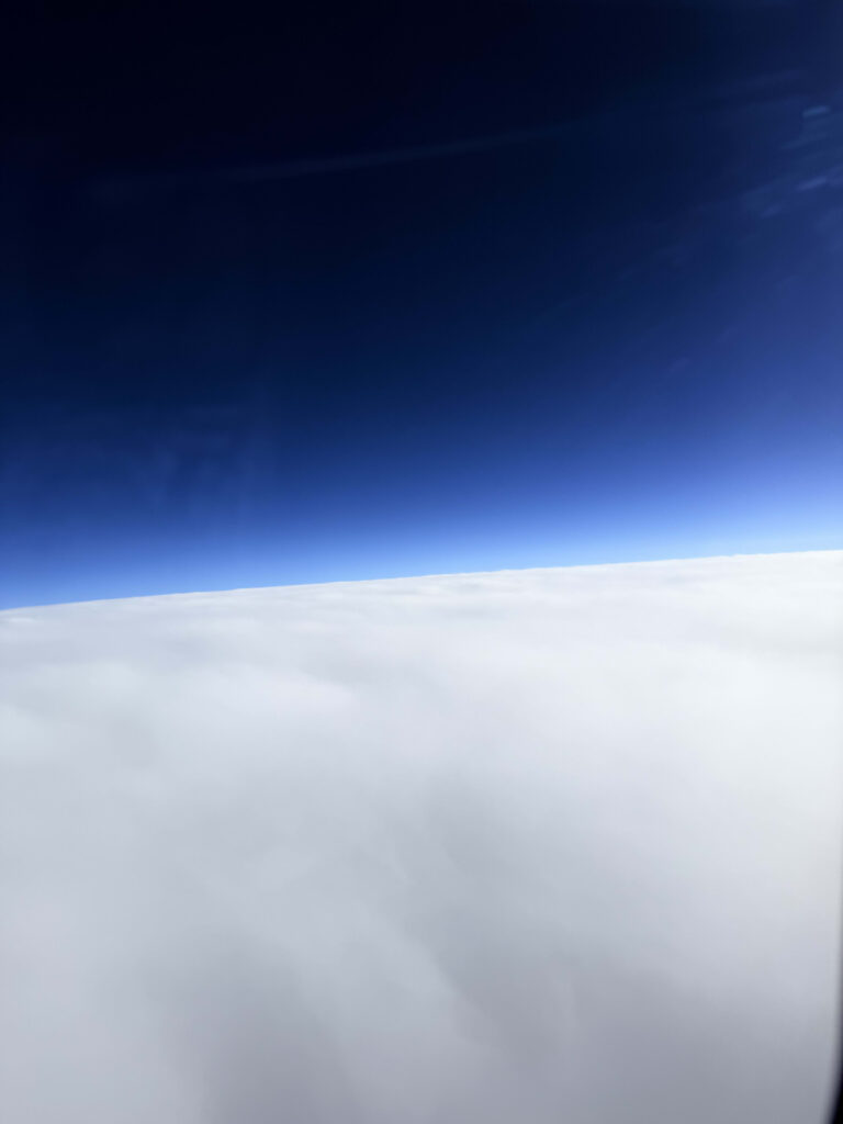 飛行機の窓から見る、深い青色の空と一面に広がる白い雲海
