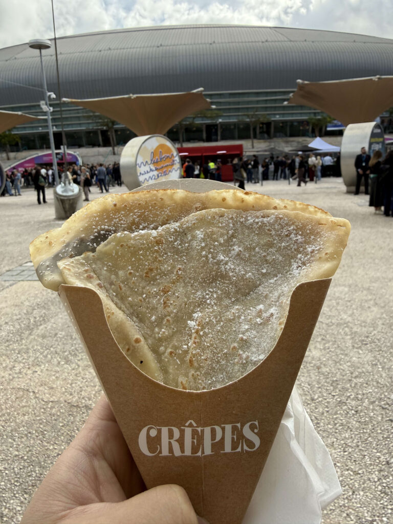 大きなアリーナを背景に、粉砂糖のかかったクレープが入った紙製のコーンを持っている手