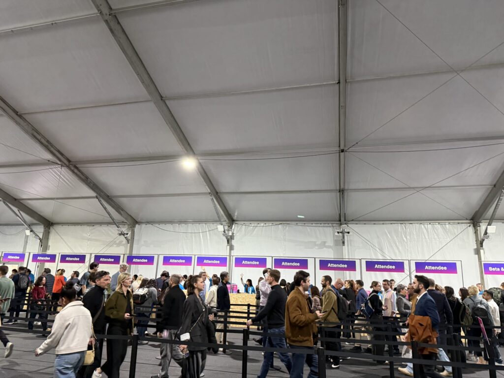 イベント会場の巨大なテント内で、「Attendee」の看板が並ぶチェックインカウンターに列を作る人々
