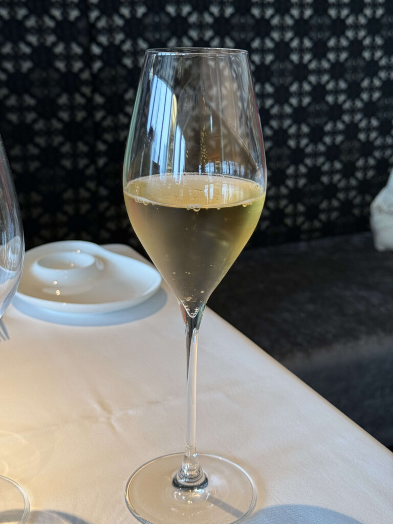A glass of golden sparkling beverage on a white tablecloth with a patterned background