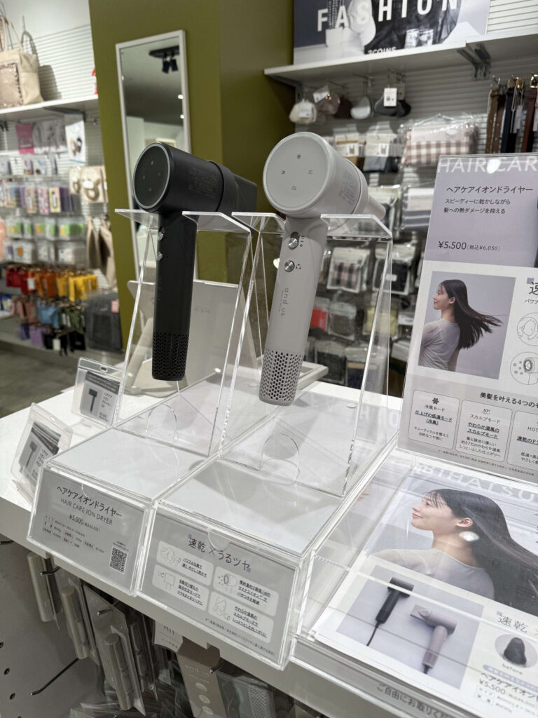 店頭にディスプレイされた「and us」ブランドのヘアケアイオンドライヤー。ブラックとホワイトの2色が並び、価格や機能説明のポップが見える。